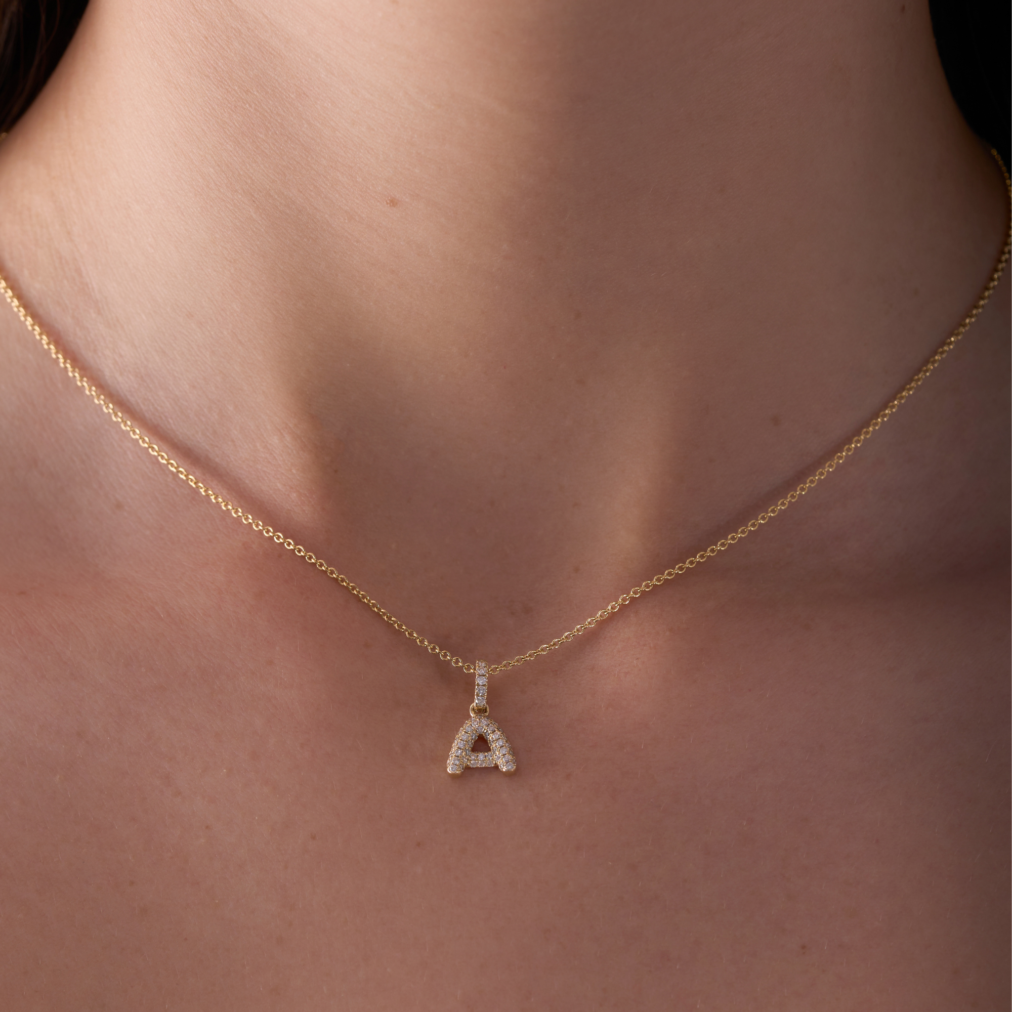 Gold necklace with a diamond-studded 'A' pendant on a person's neck.